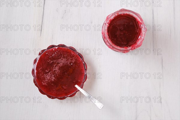 Top view of jar and saucer with cherry jam on white wooden background
