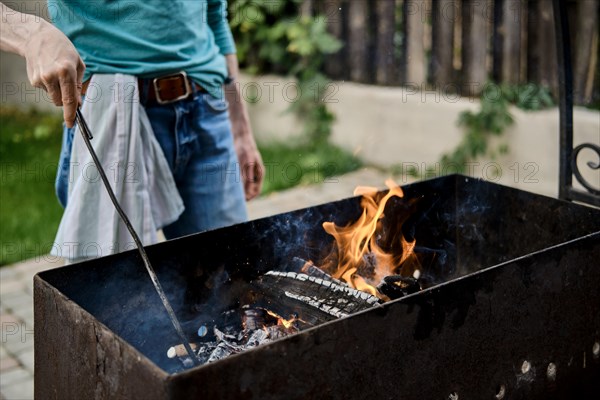 Unrecognizable man stirs the coals in the grill