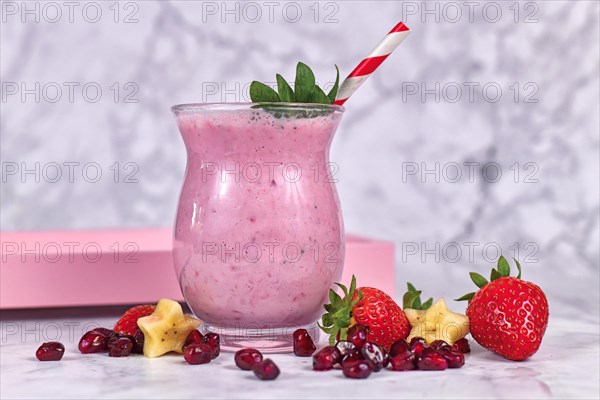 Fruit smoothie drink in drinking glass with striped straw surrounded by ingredients like strawberry