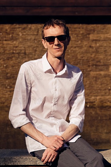 Middle age man in white shirt and sunglasses sitting in shade in hot sunny day