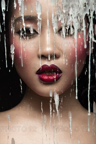 Beautiful Asian girl with bright make-up behind glass with drops of wax. Beauty face. Picture taken in the studio on a black background