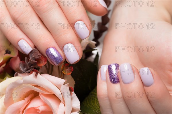 Purple neat manicure on female hands on a background of flowers. Nail design