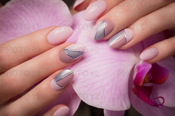 Purple neat manicure on female hands on a background of flowers. Nail design