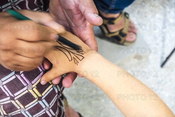 Craftsman decorating small tourist's hand in pottery factory in Fez