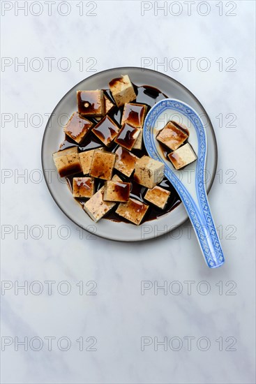 Soy sauce marinated tofu cubes in bowl with Asian ceramic spoon