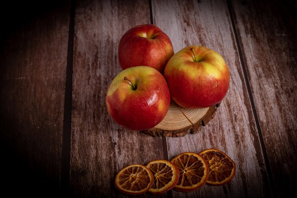 Close-up of three fresh red apples with drops of water on a slice of wood