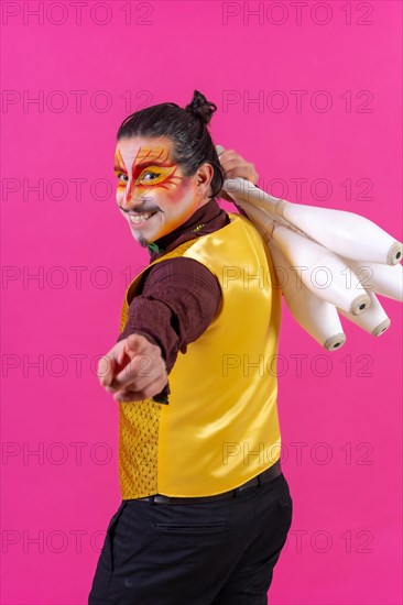 Juggler in a vest and with painted face juggling maces on a pink background