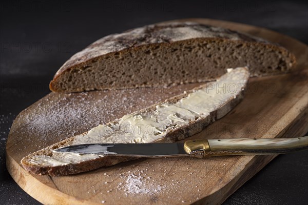 Loaf of bread on a wooden board with buttered bread