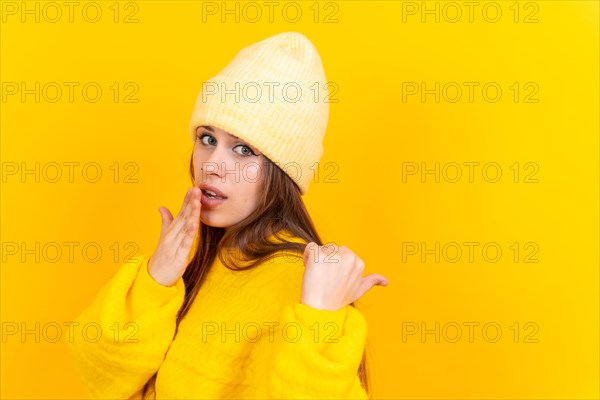 Attractive woman smiling pointing fingers at copy space on yellow background