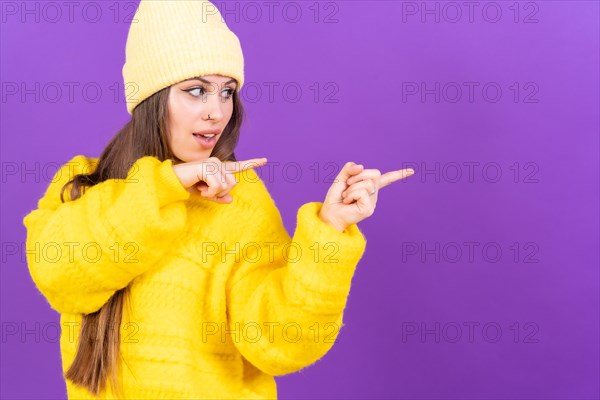 Attractive woman smiling pointing fingers at copy space on purple background