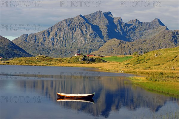 Small wooden rowboat and high barren mountains reflected in the calm waters of a small lake