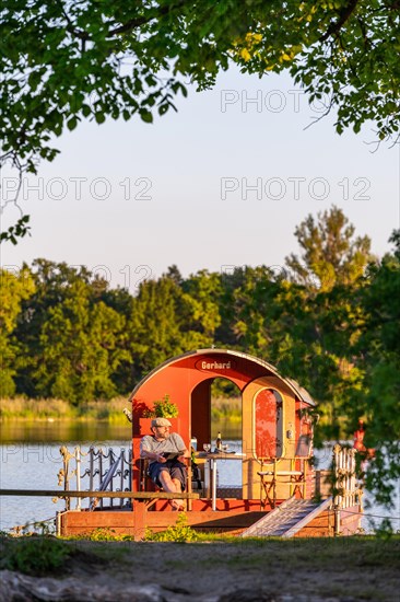 Man sitting on a houseboat, house raft, in front of the island Kiehnwerder, Breitlingsee, Brandenburg an der Havel, Havelland, Brandenburg, Germany, Europe