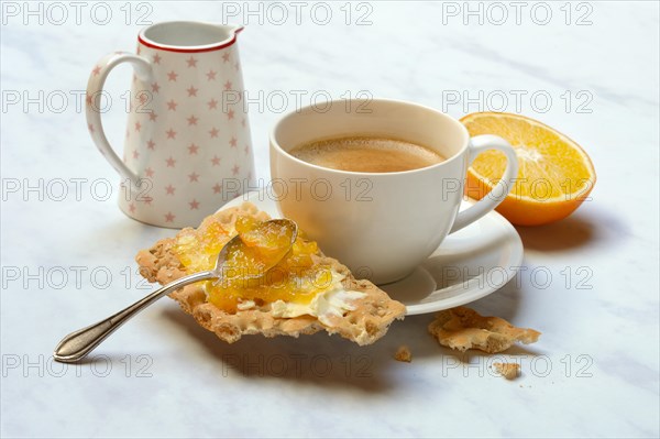 Orange marmalade in small bowls and on crispbread and cup of coffee