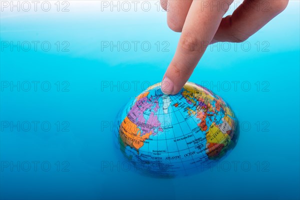 Little globe with finger on top floating in blue water