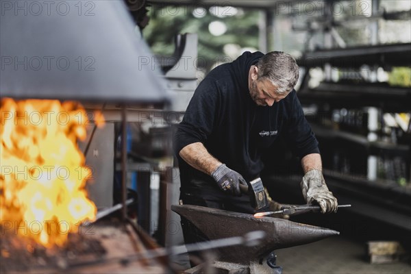 A metalworker works at the forge fire