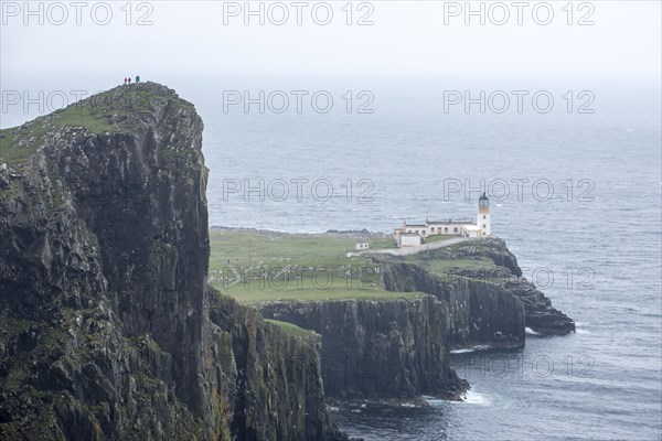 Walkers on clifftop watching Neist Point Lighthouse in the mist on the Isle of Skye