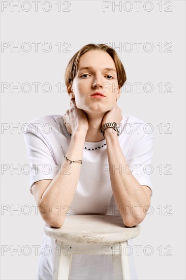 Closeup portrait of young man in white t-shirt leaning to a sit of tall chair