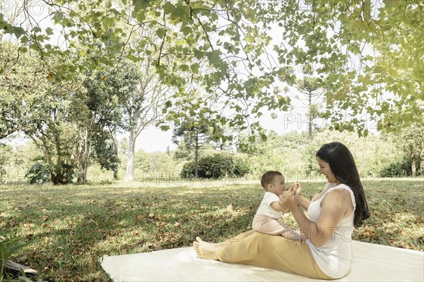 Mother and her baby daughter sitting on a blanket in a park on a sunny day. The image promotes the idea of motherhood as a joyful and fulfilling experience