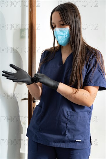 Woman doctor with mask puts on black gloves before seeing the patient