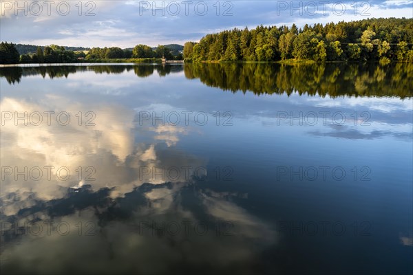 The Postfelden reservoir in the evening at golden hour. Dramatic clouds are reflected in the calm water. Hoellbachtal