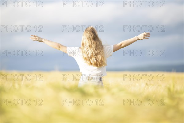 A young girl walks through a cornfield on a sunny warm day and spreads out her arms