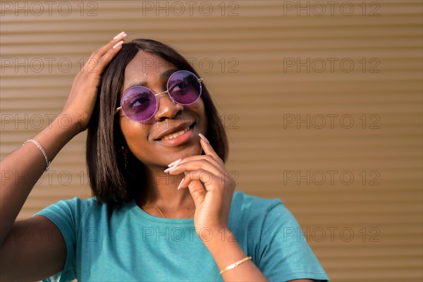 Sunny Days and Good Vibes: A Portrait of a Young Black Female Tourist Wearing Green Tee and Shades Against a Brown Wall