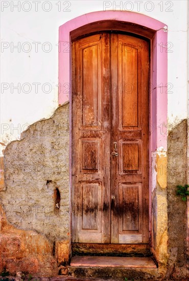 Old wooden door in colonial style mansion deteriorated by weather with damaged wall and peeled paint