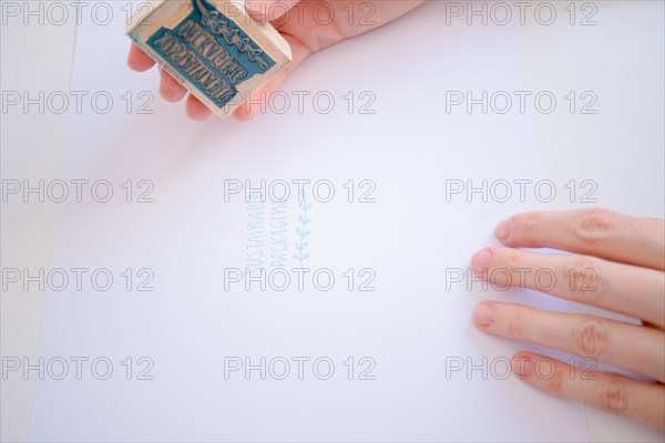 Close-up of a woman pressing a stamp with the phrase sustainable packaging on a white sheet of paper