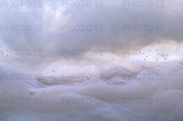 A milky cloudy bright background with floating water drops white streaks and bright spots