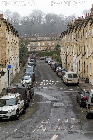 No Through Road sign written on steep road with cars parked on street