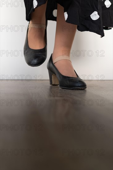 Legs of woman dancing flamenco with black clothes on wooden floor and white background