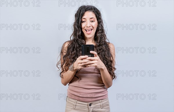 Happy and surprised girl looking at a promotion on the cell phone. Smiling woman texting with cell phone isolated. Happy latin girl using cell phone isolated