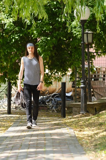 Young man with long hair in tank top and jeans walks along sidewalk