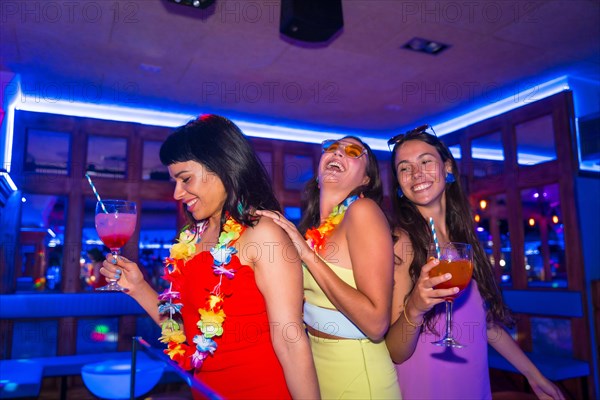 Female friends in a nightclub dancing with glasses of alcohol smiling at a night party on summer vacation