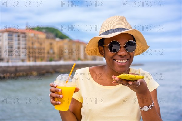 Black ethnic woman drinking orange juice texting with phone