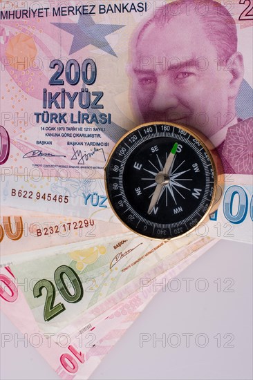 Turkish Lira banknotes by the side of a compass on white background