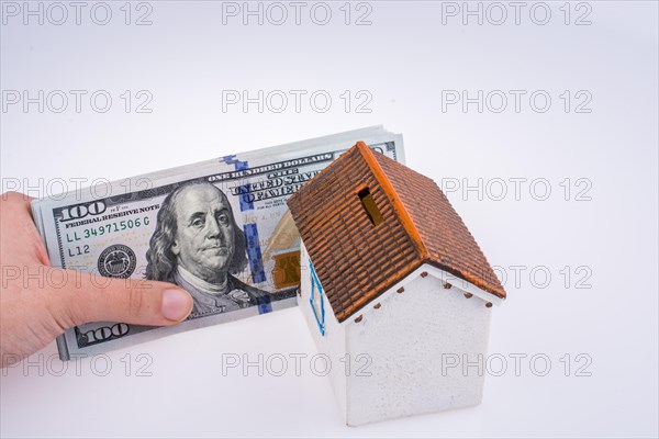 Human hand holding American dollar banknotes by the side of a model house on white background