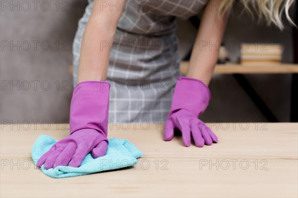 Midsection female janitor wiping wooden table with cloth