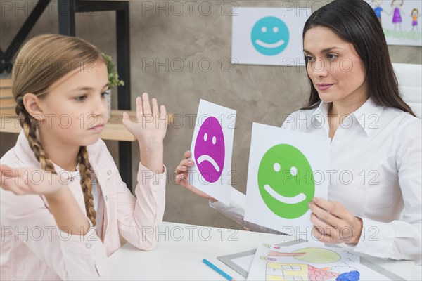 Smiling psychologist showing happy sad emotion faces cards girl child