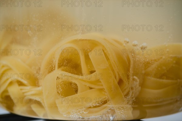 Closeup view of fettuccine pasta into boiling water in a transparent glass saucepan