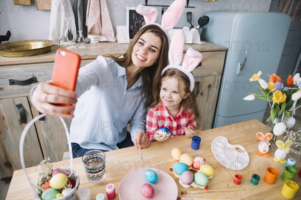 Young woman taking selfie with daughter near easter eggs