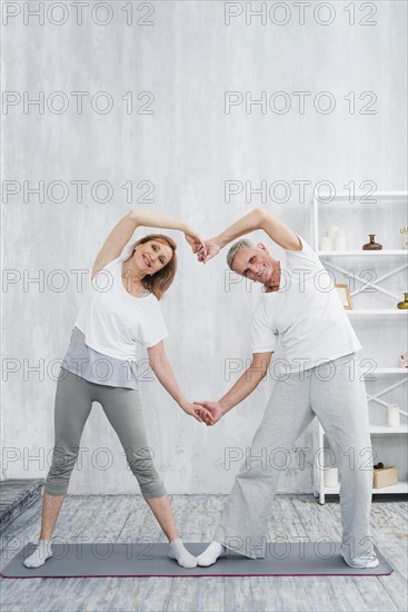 Joyful senior couple making heart shape with their hands while exercising home