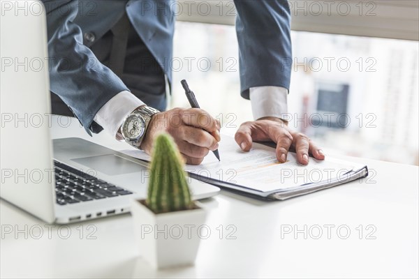 Businessman writing document with pen desk with laptop