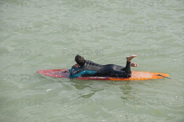 Surfer in wetsuit lying flat on his surfboard in the sea