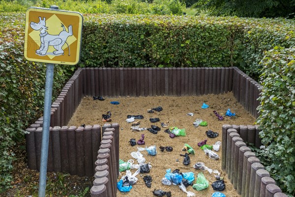 Fenced sandy public dog toilet area in city park filled with colourful discarded plastic dog poop bags