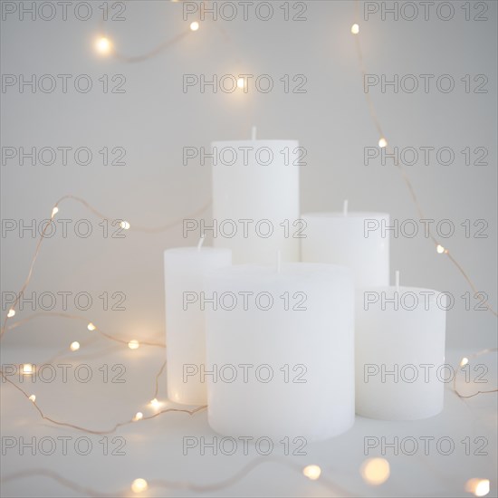 Illuminated fairy lights around white candles grey background