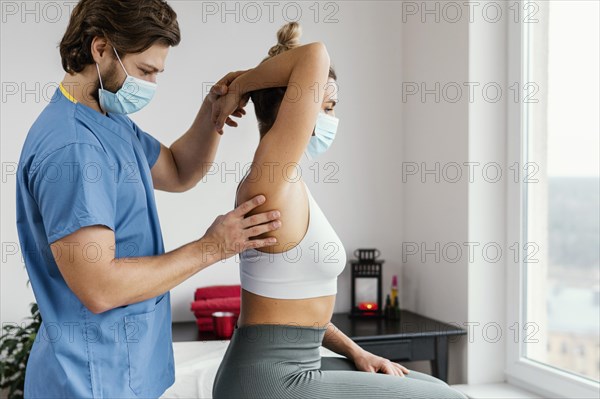 Side male osteopathic therapist with medical mask checking female patient s shoulder joint