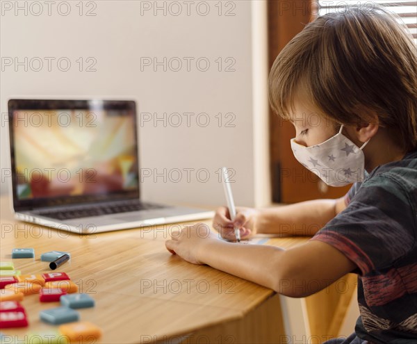 Boy wearing medical mask attending virtual school