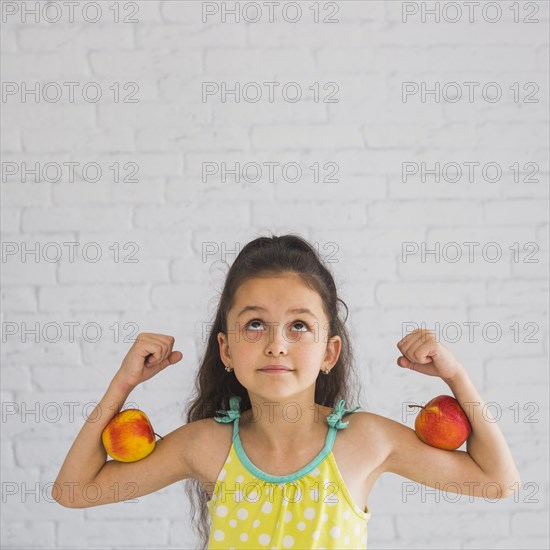 Girl flexing her hands holding apple her biceps looking up