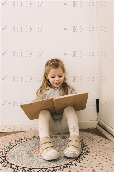Cheerful girl reading near wall